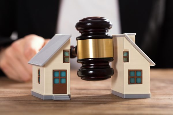 Close-up Of A Judge Striking Gavel Between Split House Over Wooden Desk